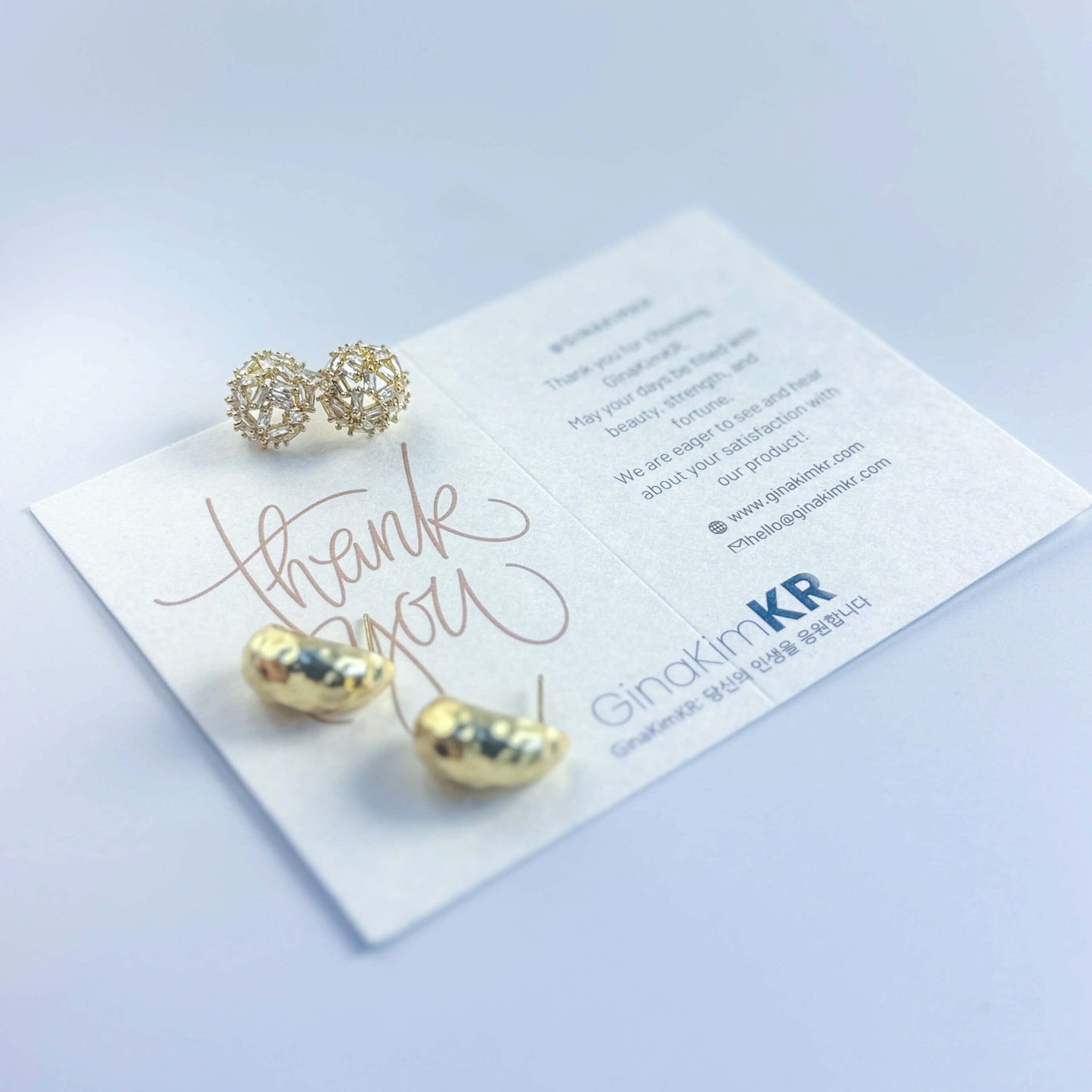 Close-up of GinaKimKR Golden Radiance earrings on white background. Highlights textured gold drop design and sparkling crystal studs.