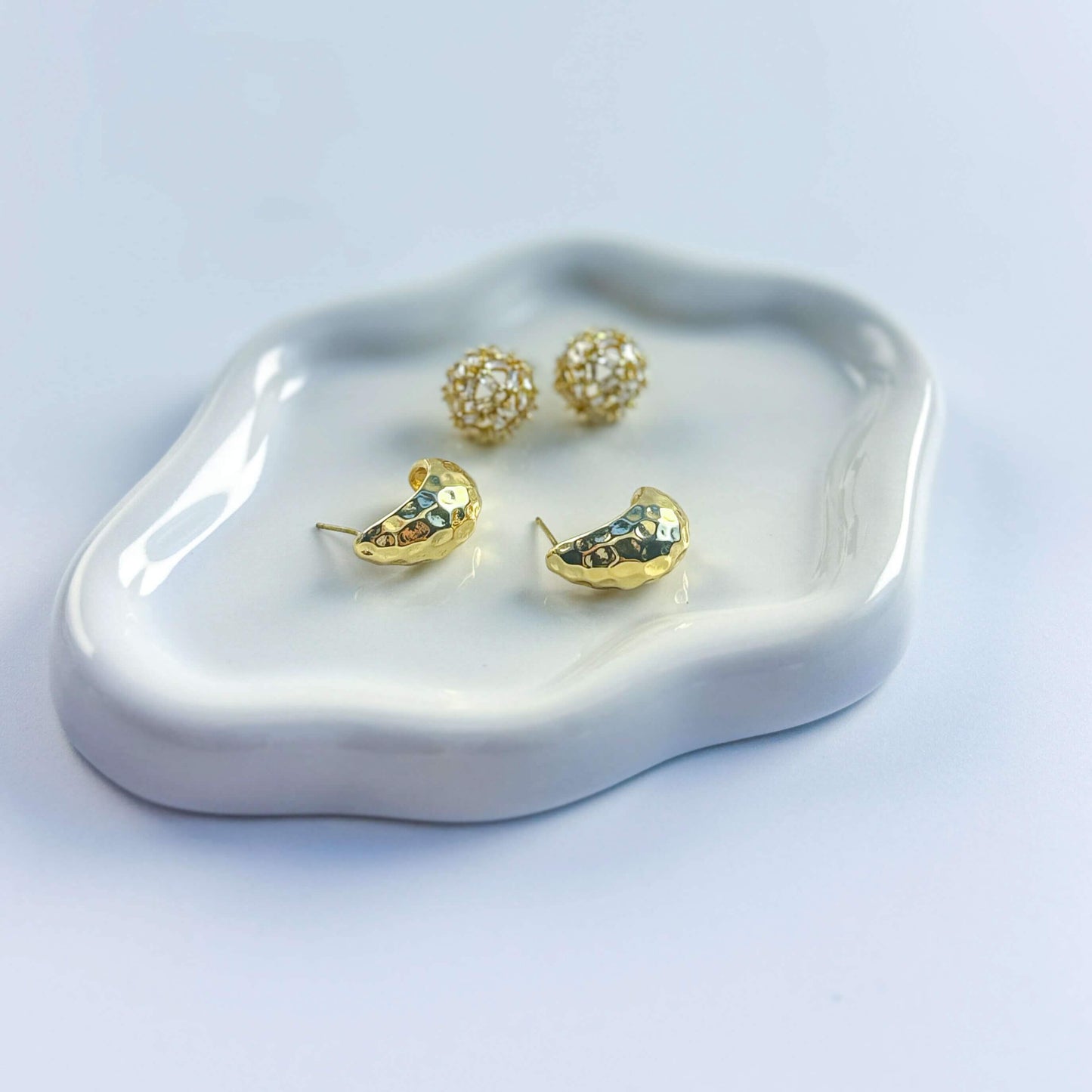 Top view of Golden Radiance earrings on display plate. Emphasizes elegant duo of hammered gold and crystal stud styles.
