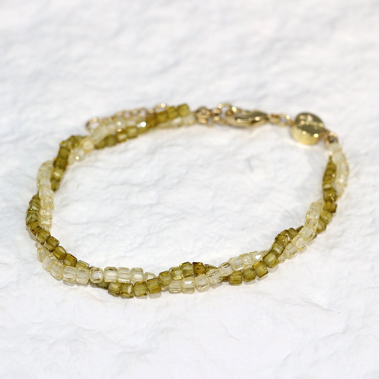 A close-up of the Olive Prism Bracelet featuring soft olive green crystal beads with a subtle shimmer. The bracelet is stretch-fit and accented with a sparkling CZ bead, worn on a woman's wrist in warm natural sunlight for a calm and elegant look.