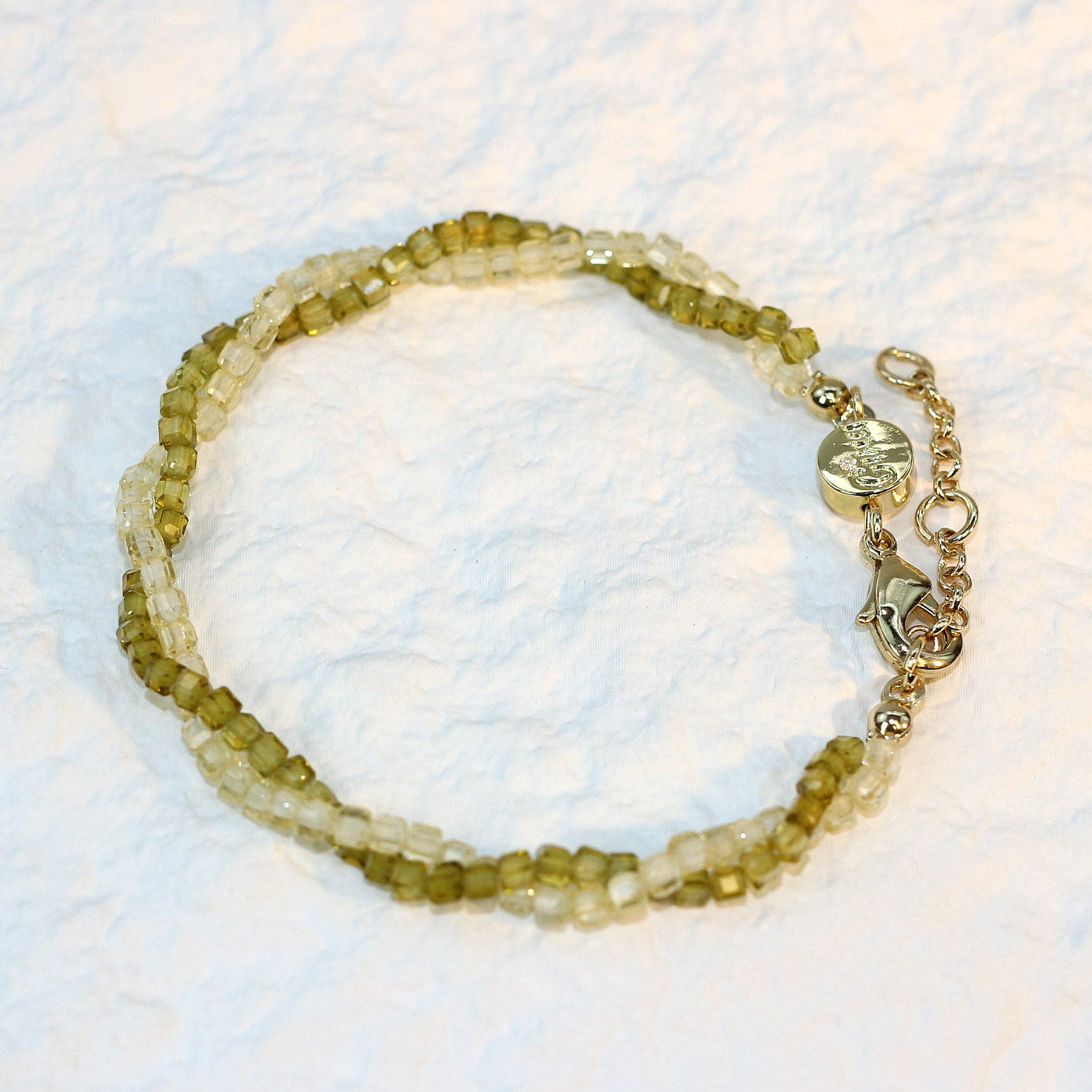 A close-up of the Olive Prism Bracelet featuring soft olive green crystal beads with a subtle shimmer. The bracelet is stretch-fit and accented with a sparkling CZ bead, worn on a woman's wrist in warm natural sunlight for a calm and elegant look.