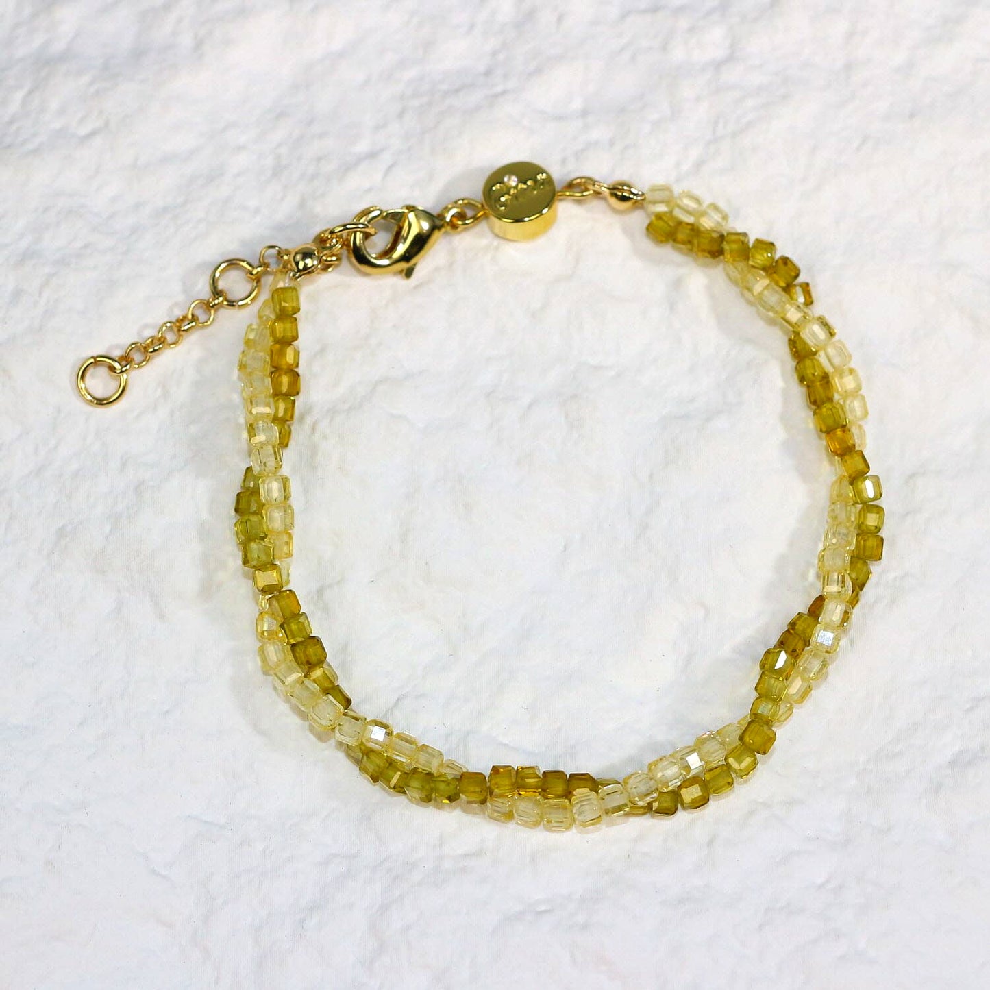 A close-up of the Olive Prism Bracelet featuring soft olive green crystal beads with a subtle shimmer. The bracelet is stretch-fit and accented with a sparkling CZ bead, worn on a woman's wrist in warm natural sunlight for a calm and elegant look.