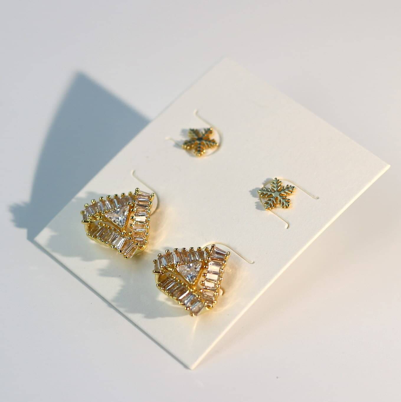 Flat lay of Snow Prism Earring Set in soft gold tone, shown on angled white packaging for gifting.