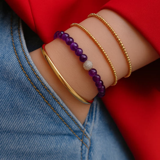 A woman wearing the Amethyst Fortune Bracelet by GinaKimKR, featuring purple amethyst stones, gold detailing, and the signature logo charm. Peaceful and stylish.