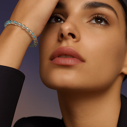 A woman’s wrist styled with a delicate Aqua Clarity Bracelet made of 4mm crystal quartz beads and turquoise accents, highlighting its minimal and transparent sparkle against a refined look.