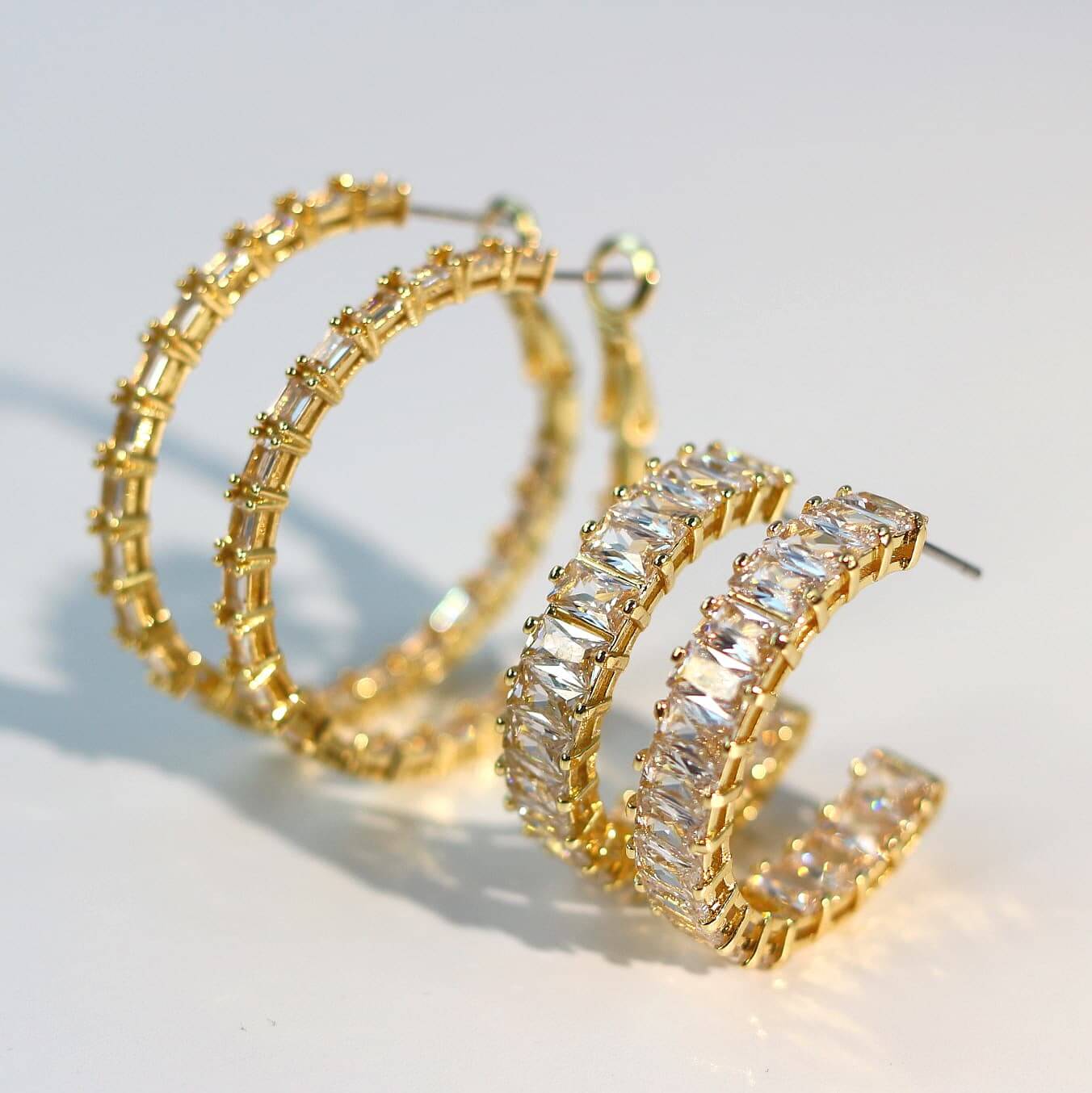 Side-by-side comparison of two gold hoop earrings: the Linear Radiance Earrings with slim baguette CZ layout (left), and the Celeste Crown Earrings with full-set wide CZ design (right).