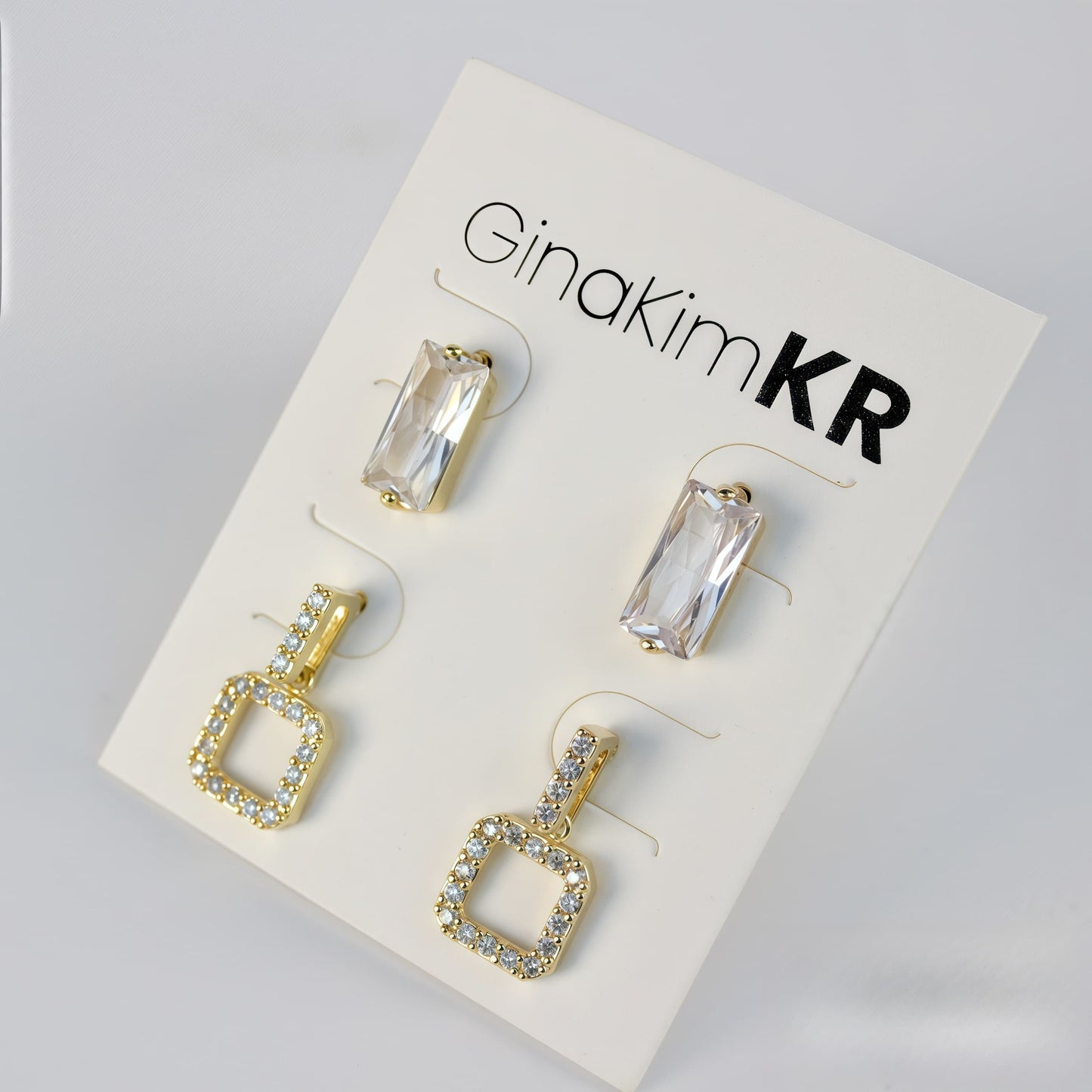 Bright-lit front shot of GinaKimKR earring set with gold pavé square drops and clear crystal-cut studs