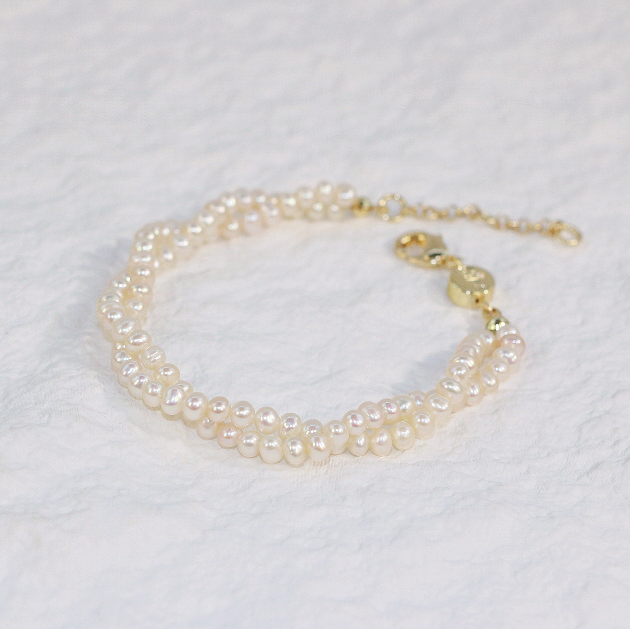 Close-up of Double Grace Pearl Bracelet featuring two rows of lustrous freshwater pearls, braided with a gold clasp and extender for a refined, luxurious finish.