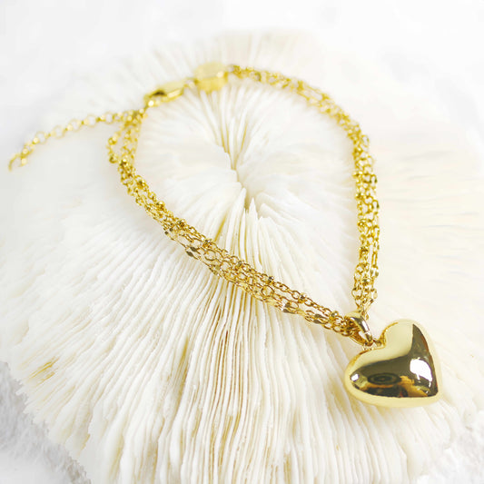 Elegant gold heart bracelet with triple chain design displayed on textured background