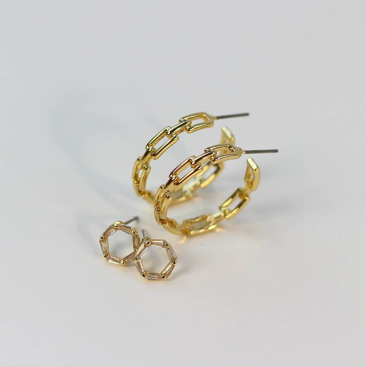 Angled view of Geo Spark Earring Set showing the sparkle of trapezoid CZ crystals and geometric cut-out gold hoops on a neutral background.