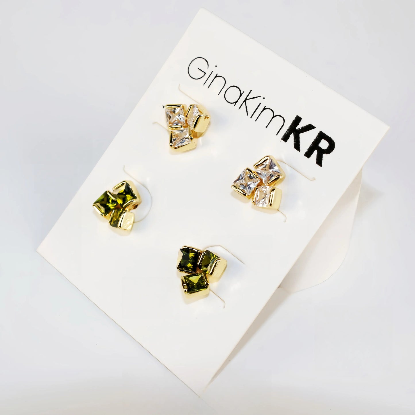 Flat lay image of Geo Trio Earring Set with three pairs of studs in clear and olive green, arranged in rows.