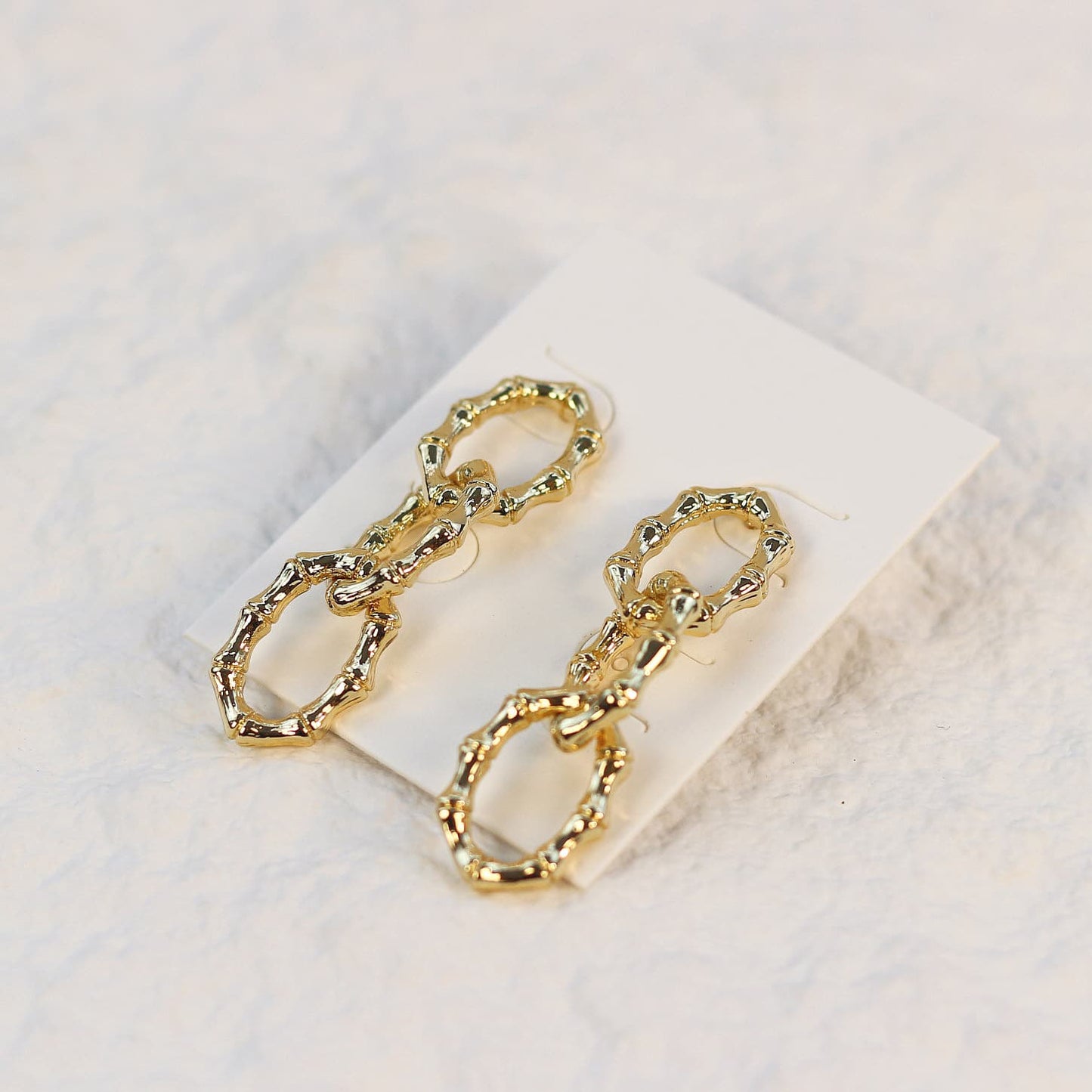 Angled shot of Bamboo Link Drop Earrings showing gold oval links with a polished bamboo finish on a soft cream-colored card.