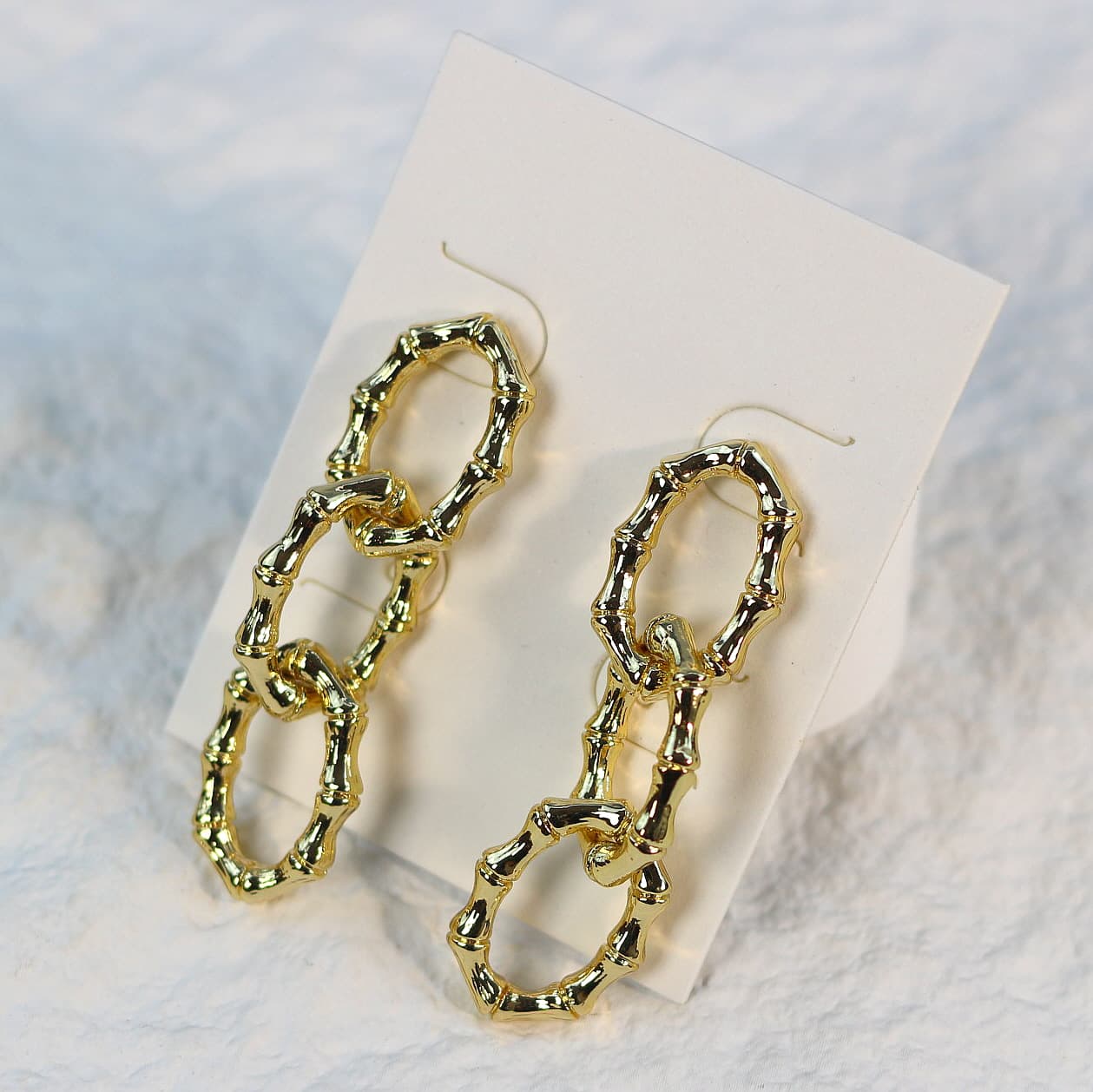 Close-up of gold bamboo link earrings, emphasizing the organic oval shapes and warm tones, presented on a cream background.