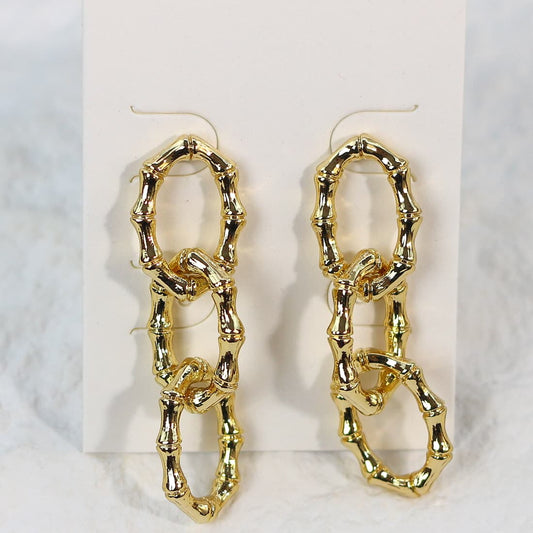 Front-facing view of bamboo-style gold drop earrings featuring three textured links, arranged symmetrically on a cream display card.