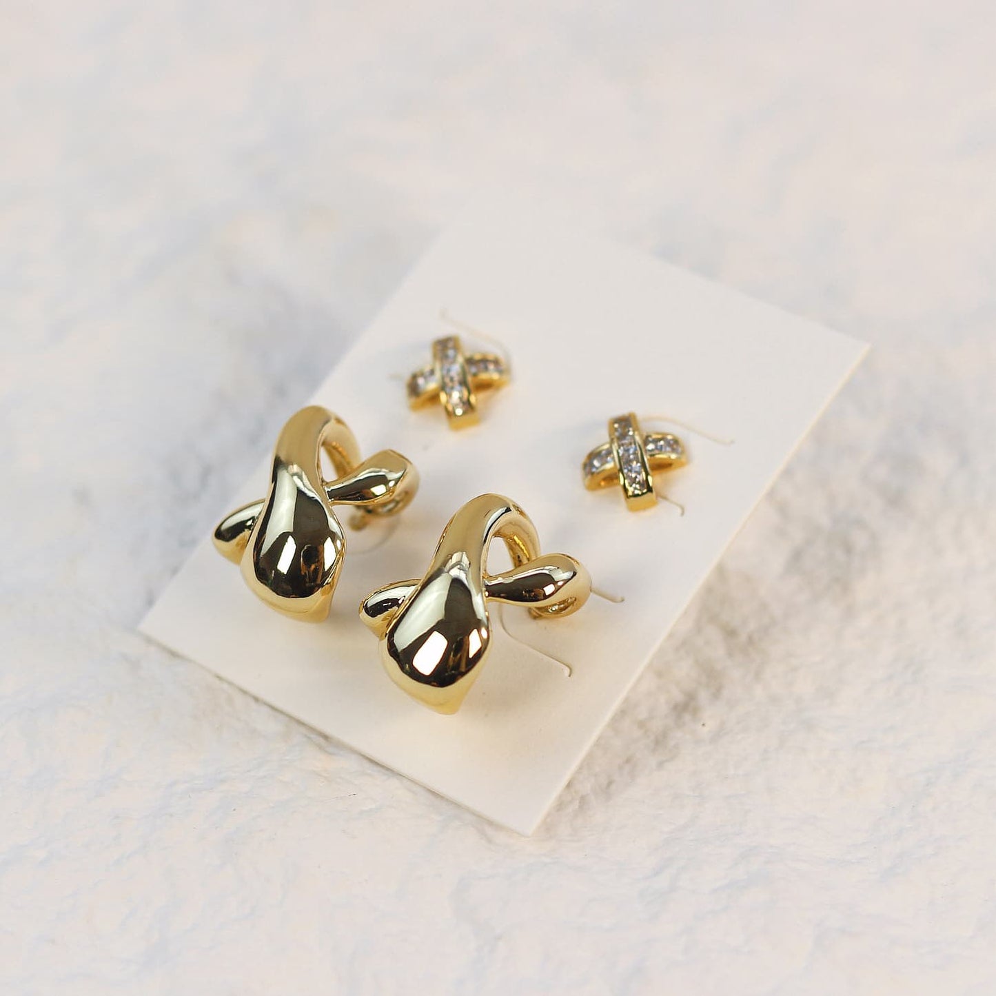 Top-down product view of Eternal Flow Earring Set, with asymmetrical gold curves and sparkling 9.6mm CZ studs placed on a white card.