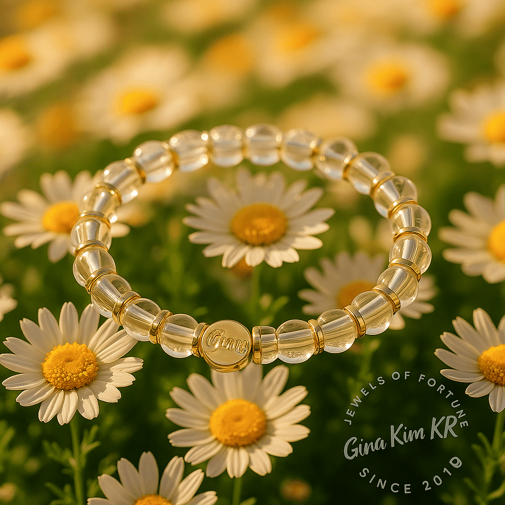 A crystal quartz stretch bracelet with gold accents and a round GinaKimKR logo tag, displayed on white daisies under warm sunlight. Natural, radiant, and serene.