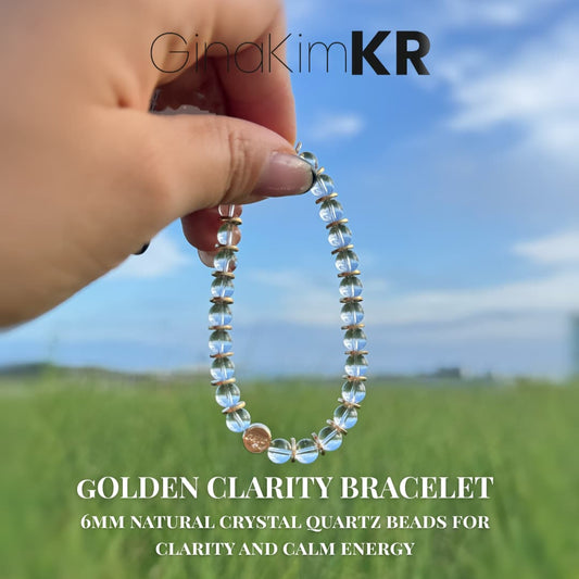 A hand holding the Golden Clarity Bracelet by GinaKimKR, made with 6mm natural crystal quartz beads, photographed outdoors with a clear blue sky and green field. Ideal for gemstone jewelry lovers seeking clarity and calm energy.