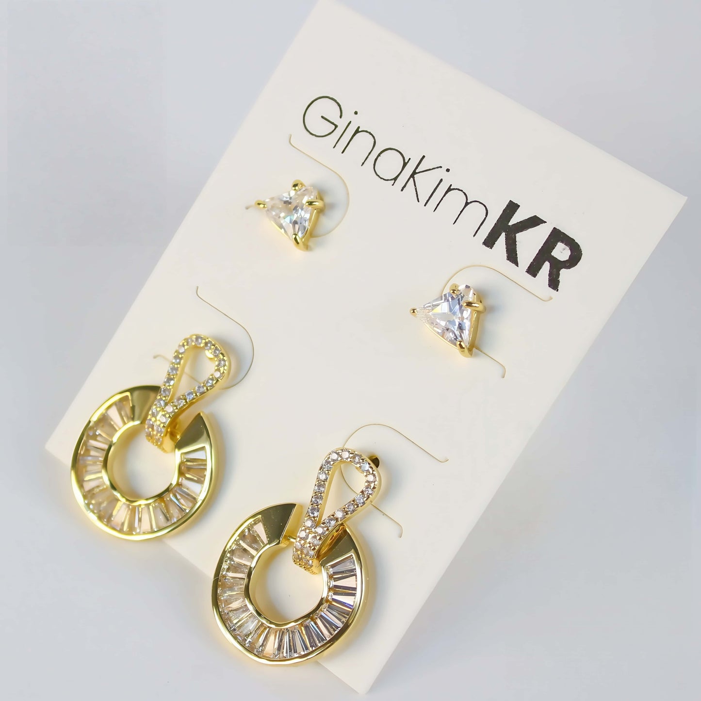 Golden Edge Duo by GinaKimKR – Elegant 2-pair earring set with triangle CZ studs and baguette crystal gold loop drops, shown on brand card