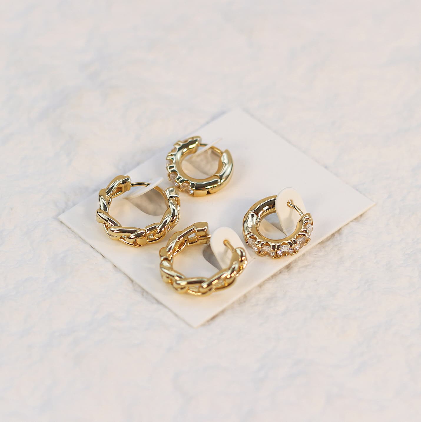 Soft-lit image of Golden Gleam Huggie Set highlighting mixed gold finishes and cubic zirconia sparkle, presented on a clean white card.