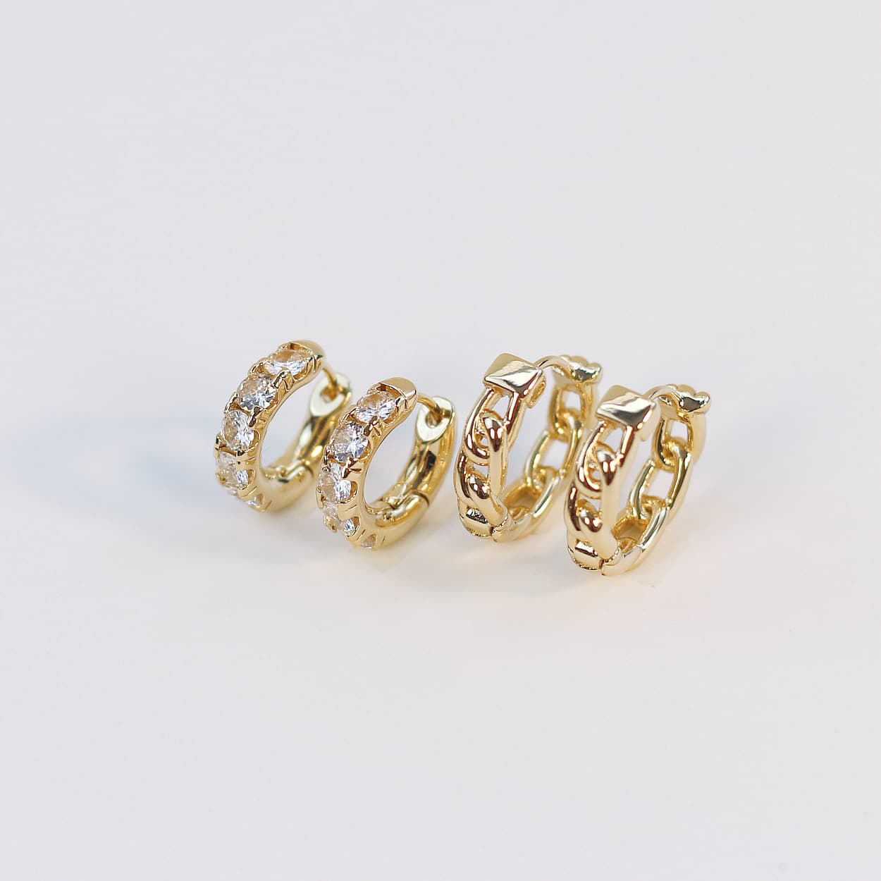 Side view of Golden Gleam Huggie Set featuring four gold hoop styles, including crystal and braided designs, arranged on a textured white background.