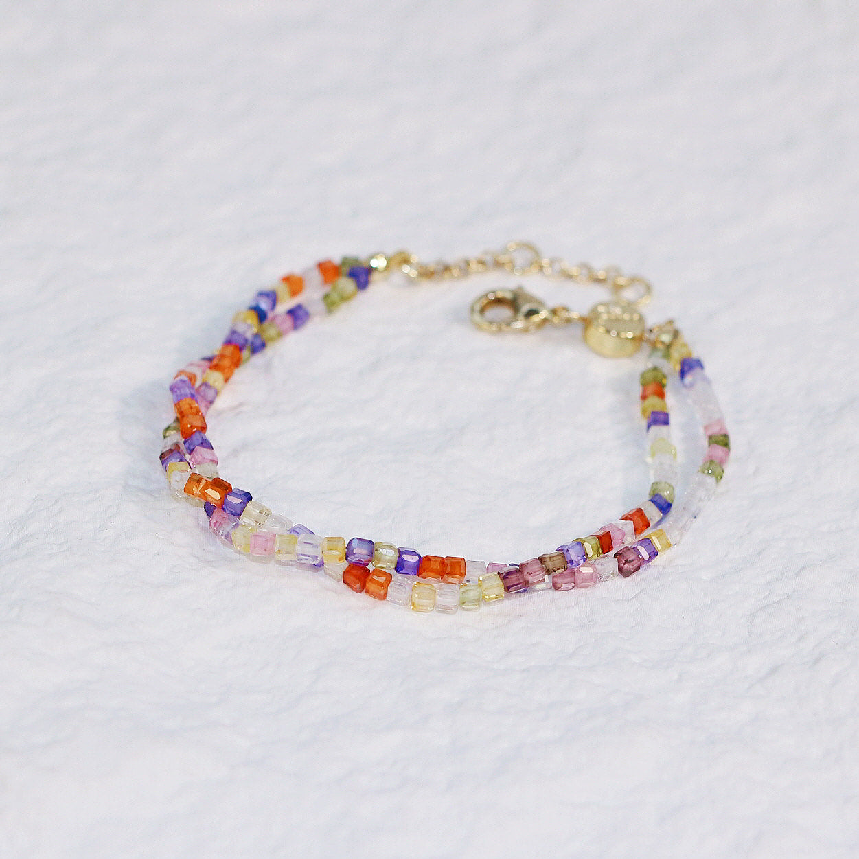 GinaKim Joy Prism Bracelet on wrist, featuring a vibrant mix of colorful cubic beads with a white shell button clasp, adding a touch of elegance and sparkle. Perfect for daily wear and casual chic style.