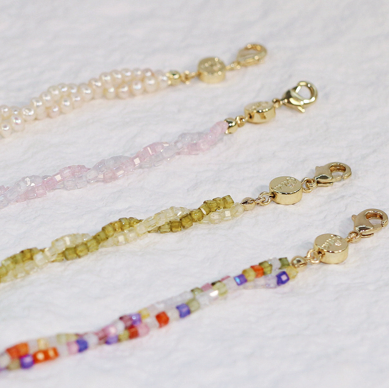 Angled close-up of four bracelets—Joy, Olive, Blush Prism, and Double Grace Pearl—showcasing cubic zirconia sparkle and soft pastel hues, styled for a refined and elegant look.