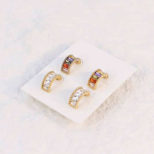 Lumière Arc Earring Set displayed on a cream card, featuring two pairs of curved post earrings in gold—one with clear CZ baguettes, the other with multicolor crystals.