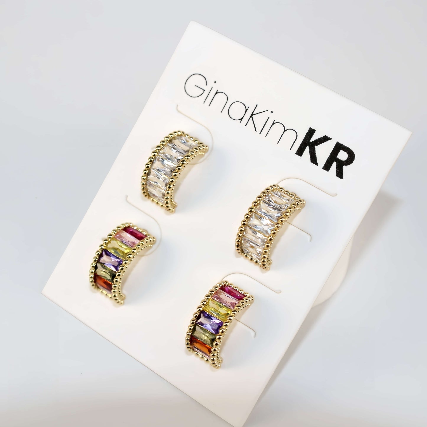 Product card featuring Lumière Arc Earring Set under warm lighting, with both crystal-accented gold pairs displayed front-facing.