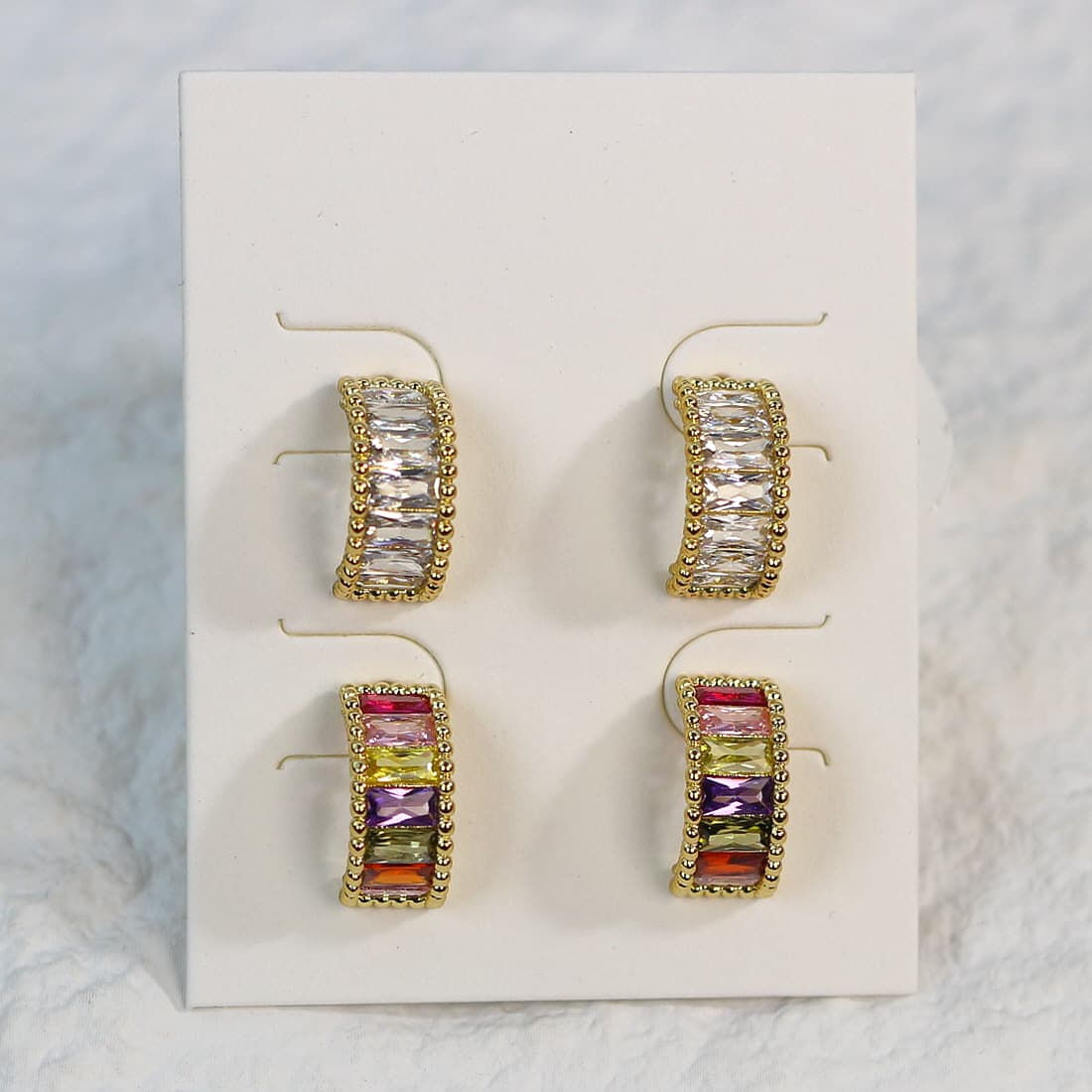 Top-down view of Lumière Arc Earring Set, showing symmetrical placement of two gold curved earrings sets—one sparkling clear, one vibrant multicolor.