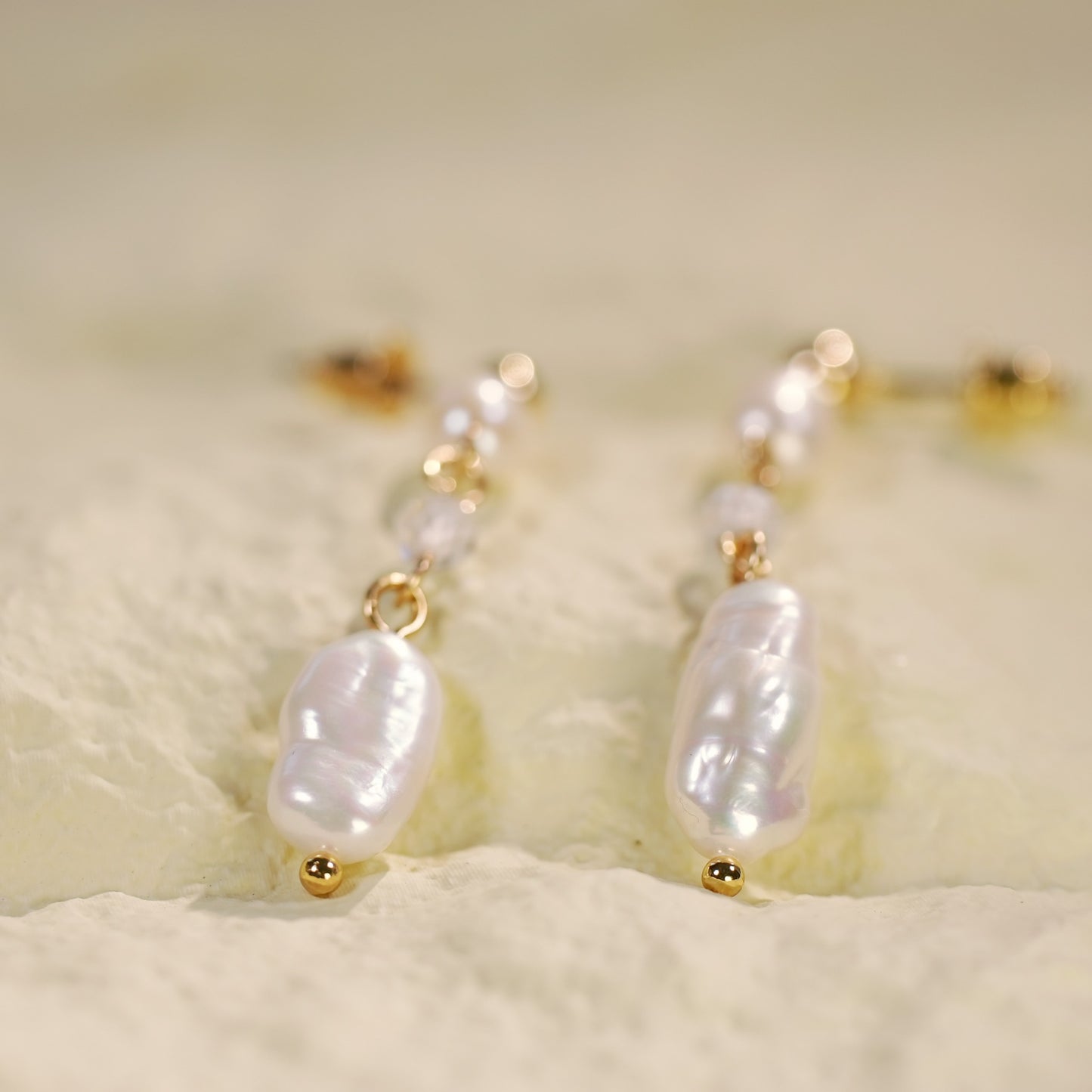 Detailed view of GinaKimKR’s baroque pearl drop earrings with uneven freshwater pearls and 14K gold-plated accents, laid out on a softly lit background.