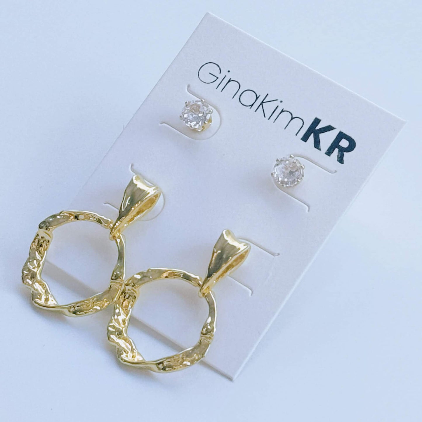 Flat lay image of GinaKimKR Molten Circle Earring Set showing gold textured hoops and CZ studs on white background