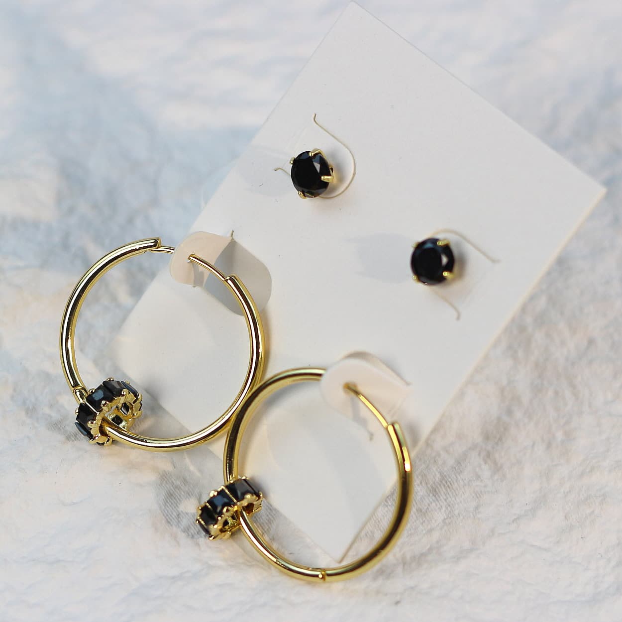 Soft daylight view of Noir Balance Earring Set on a cream card, emphasizing the contrast between jet crystals and polished gold hoops.