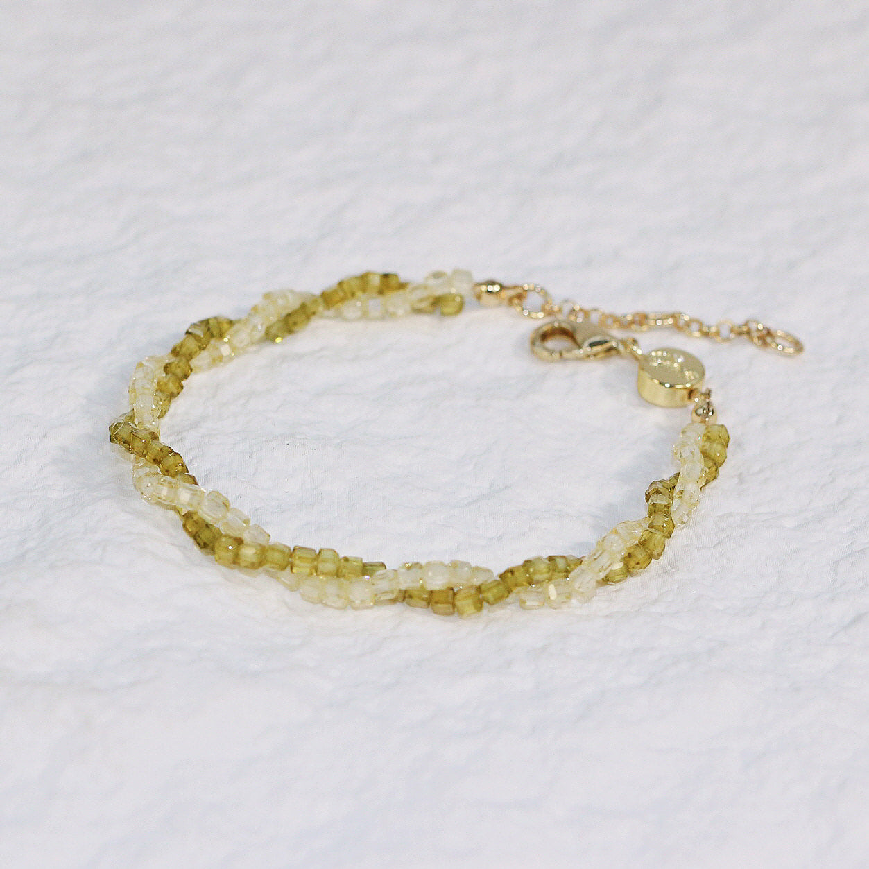 Close-up of Olive Prism Bracelet featuring light green and clear square CZ beads, braided with a gold clasp and extender, adding natural sparkle to any outfit.