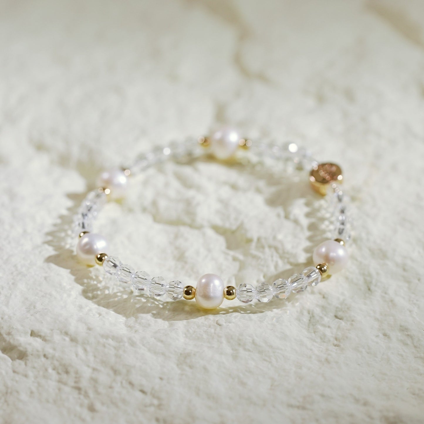 Stretch bracelet featuring five natural freshwater pearls and faceted crystal quartz beads, accented with gold-plated spacers and GinaKim’s signature logo tag. Softly elegant and handmade.