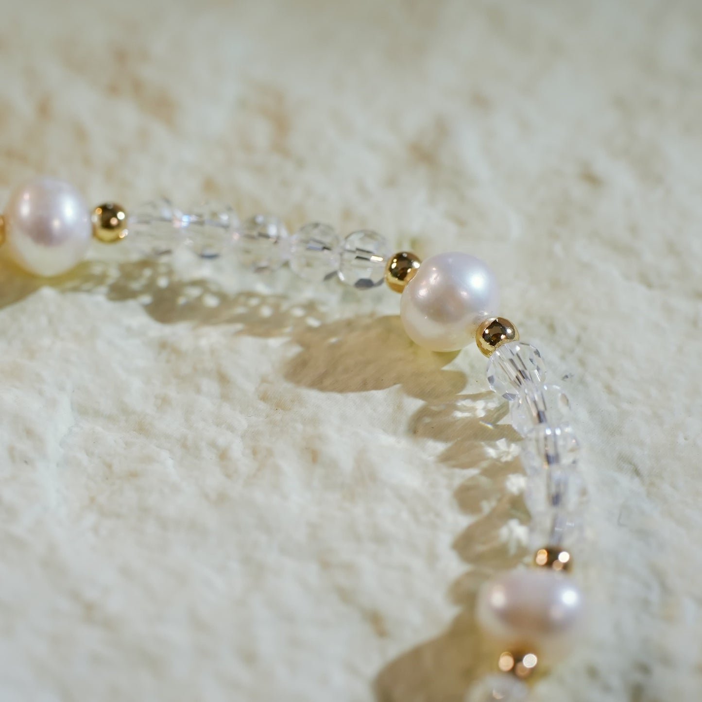 Flat-lay view of the Crystal Pearl Whisper Bracelet highlighting freshwater pearls, crystal quartz, and gold accents on a softly lit neutral background. Signature GinaKim tag visible.