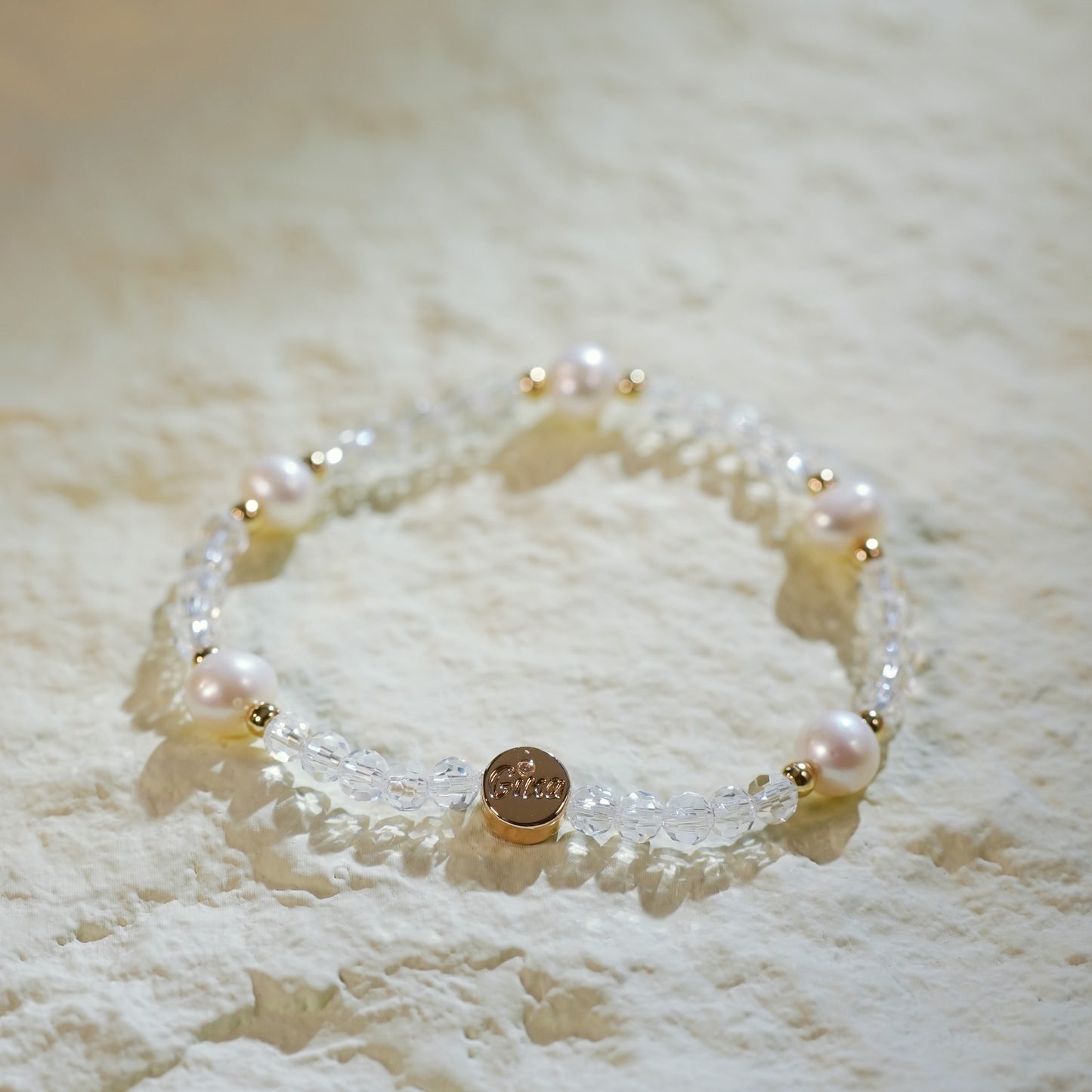 Close-up of the Crystal Pearl Whisper Bracelet showcasing the delicate mix of five pearls, crystal quartz beads, and handmade gold-plated spacers with a branded logo charm.