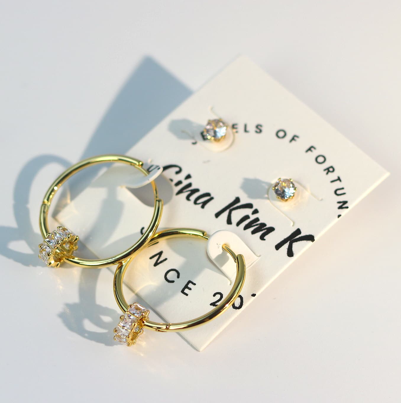 Radiant Harmony Earring Set shown with side lighting, emphasizing gold hoop texture, clear CZ studs, and shimmering crystals on a cream background.