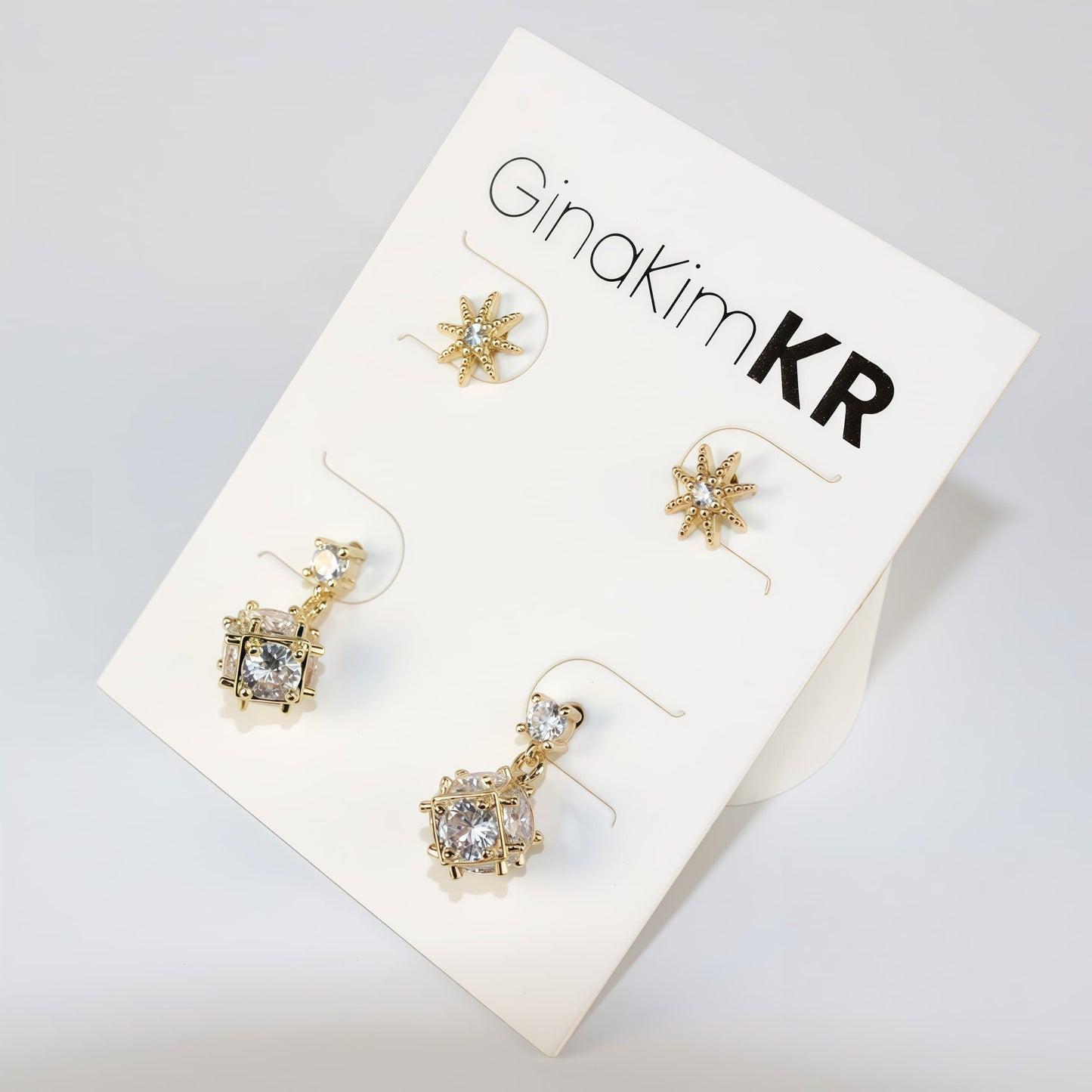 Top view of Starlume Earring Set with gold star studs and dimensional drop earrings, arranged on white card.