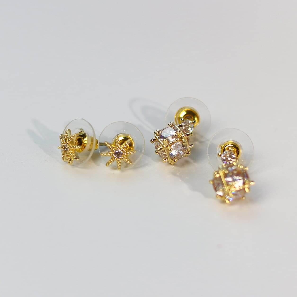 Side-angled image of Starlume Earring Set showcasing star studs and gold cage-style CZ drops.