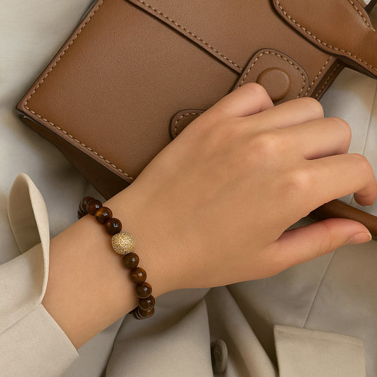 A person wearing the Tiger’s Eye Fortune Bracelet by GinaKimKR, featuring shimmering tiger’s eye stones and gold accents. Strong and stylish.