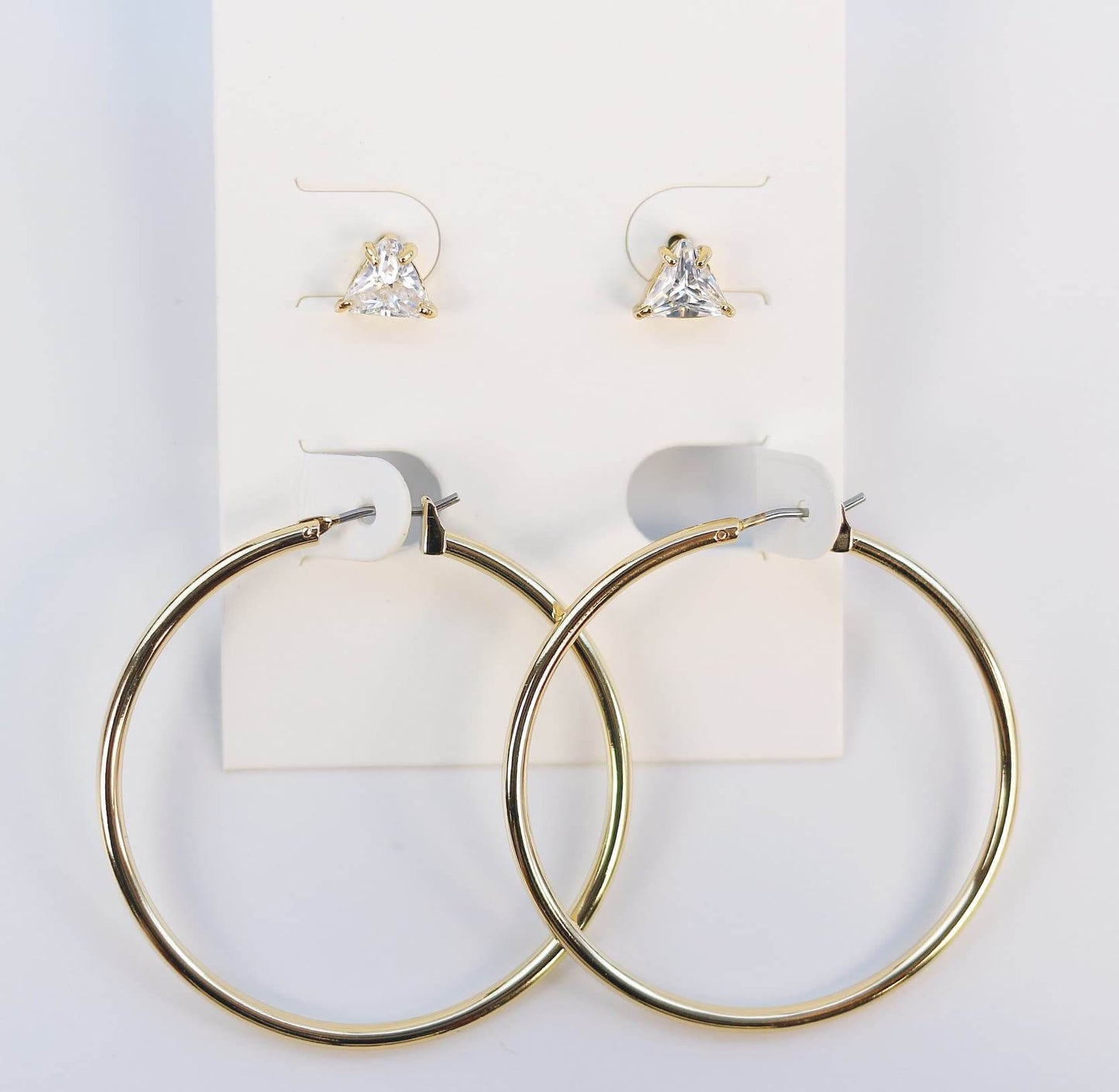 Front-facing Triad Glow Earring Set on a cream card, featuring 6mm triangle-cut CZ studs and statement 42mm gold hoops with post-back design.