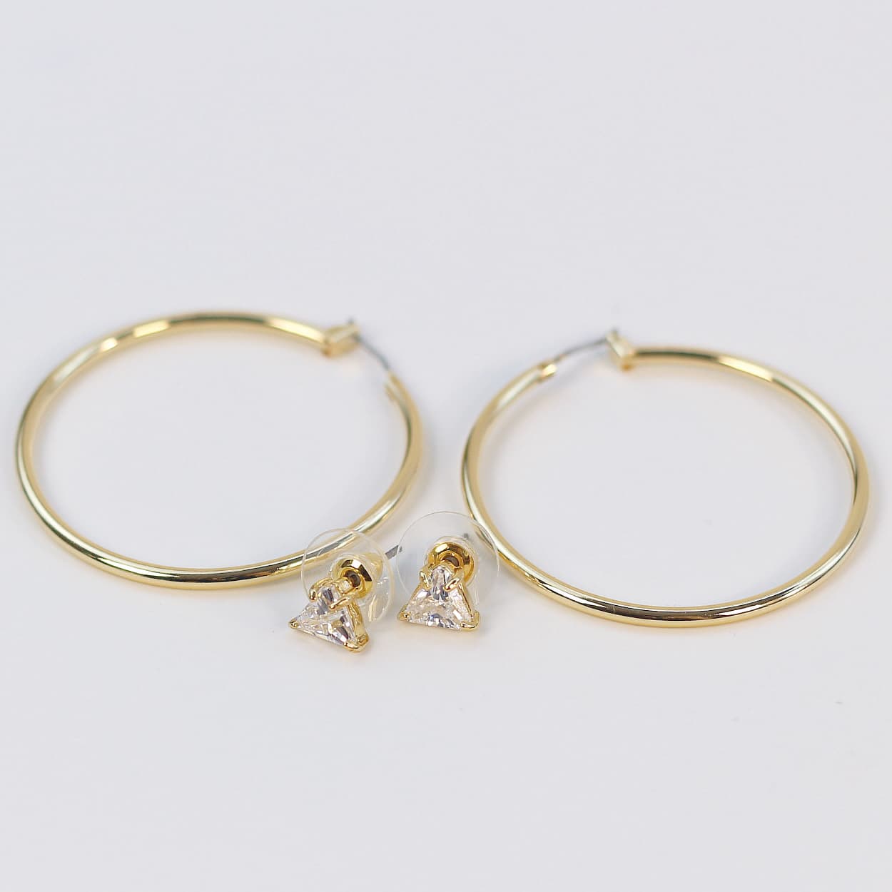 Side-angled view of Triad Glow Earring Set showing triangular CZ studs and oversized 42mm gold hoops with subtle reflections on a cream-colored card.