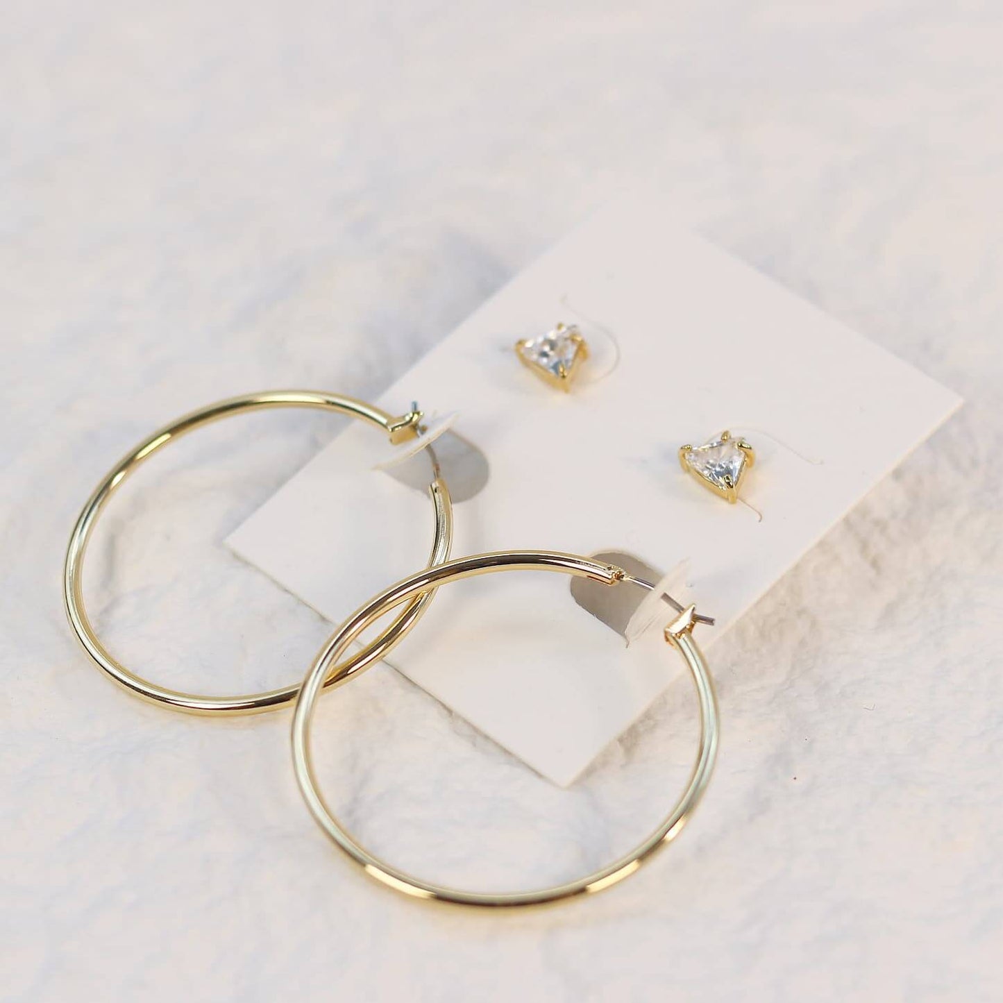 Triad Glow Earring Set with triangular 6mm CZ studs and large 42mm gold hoops with post-back closures, displayed on a cream card with soft front lighting.