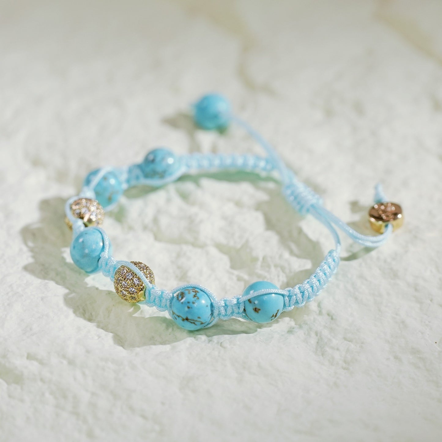 Handmade turquoise macramé bracelet featuring natural turquoise beads and gold-plated CZ accents, with adjustable sliding knot and GinaKim branding. Displayed in a satin-lined gift box.