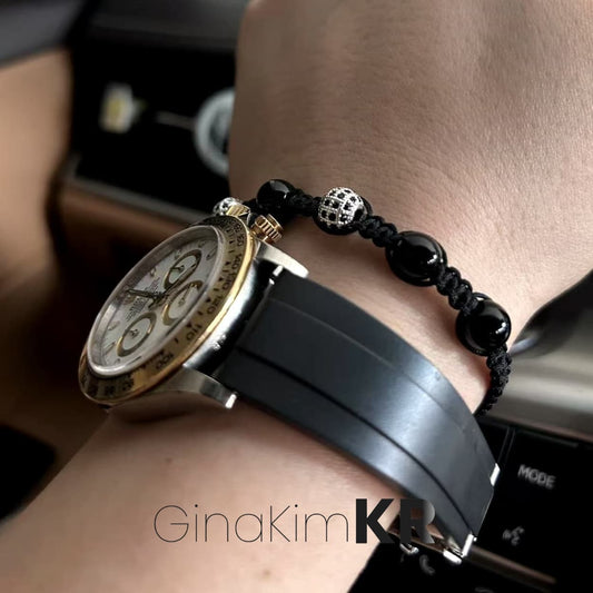 A man’s wrist wearing the Shadow Guard Bracelet by GinaKimKR, featuring black onyx beads and silver CZ accents in a hand-tied macramé design, styled next to a luxury gold watch.