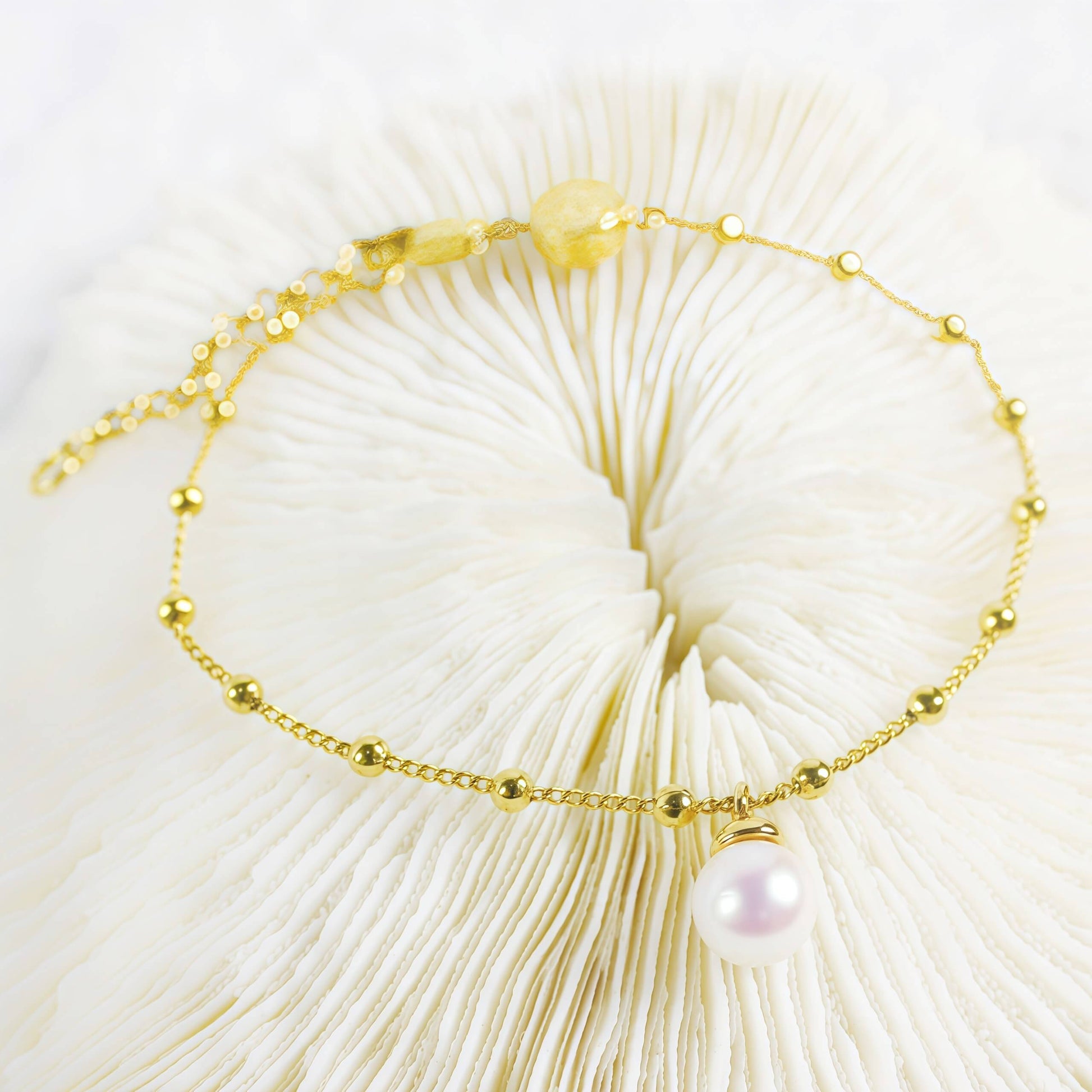 Elegant gold bracelet with delicate chain, small gold beads, and a single pearl charm