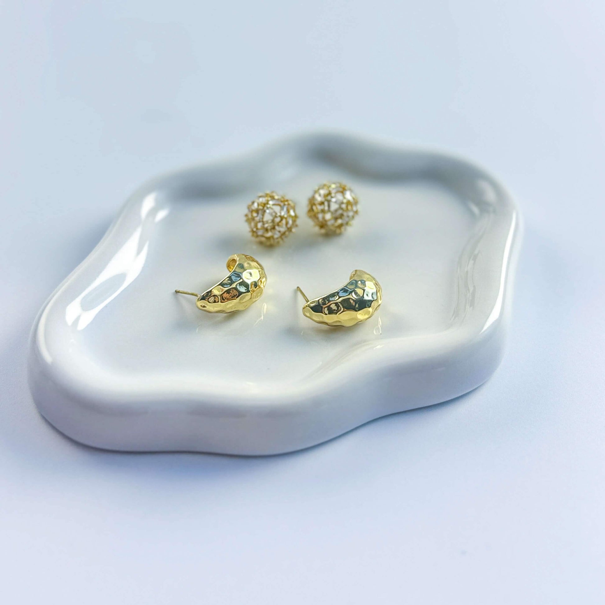Top view of Golden Radiance earrings on display plate. Emphasizes elegant duo of hammered gold and crystal stud styles.
