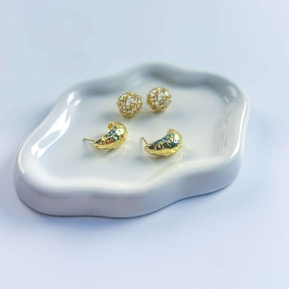 Top view of Golden Radiance earrings on display plate. Emphasizes elegant duo of hammered gold and crystal stud styles.
