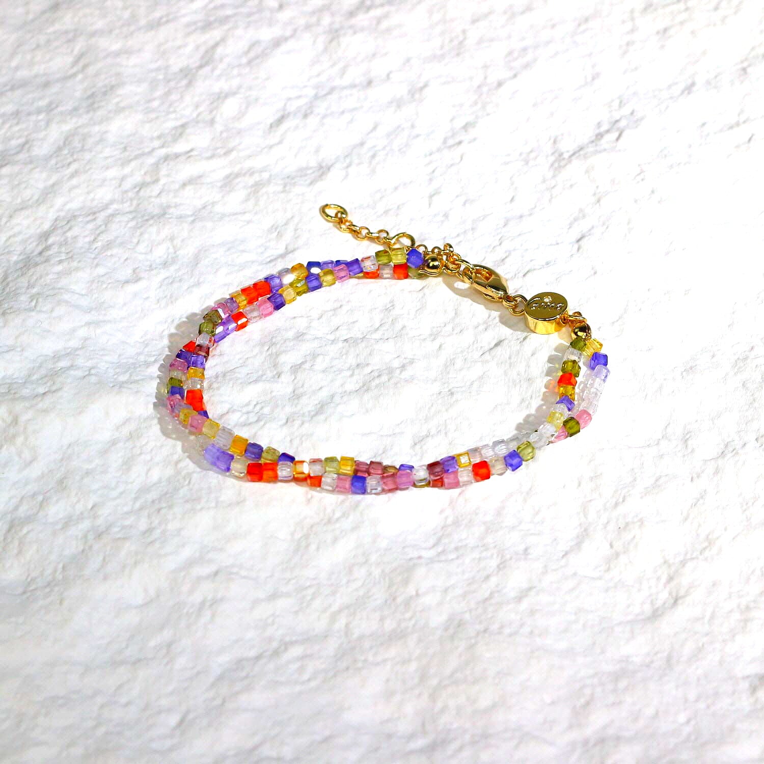 A close-up of the Joy Prism Bracelet featuring soft blush-toned crystal beads with a subtle iridescent sheen. The bracelet is stretch-fit and accented with a delicate CZ bead, styled elegantly on a woman's wrist in natural sunlight.