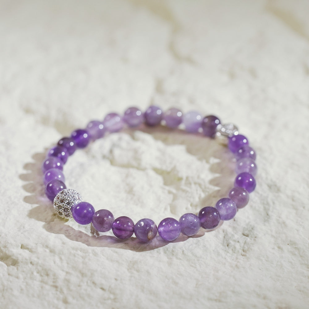 A handmade Korean amethyst fortune bracelet with deep violet beads, a gold-plated CZ accent, and a GinaKimKR logo charm. Calming and elegant.