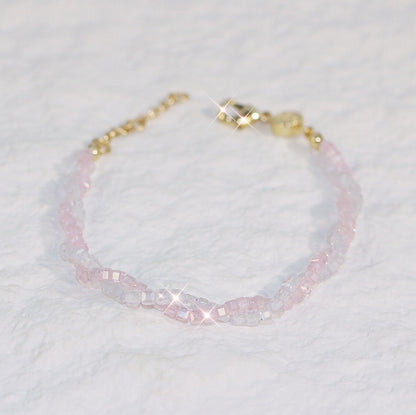 Flat-lay view of the Blush Prism Bracelet showing braided pink and clear cubic zirconia beads with a gold clasp and extender, displayed on a neutral surface.